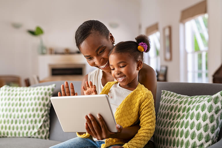 image of smiling mother and young daughter on her lap looking at a tablet