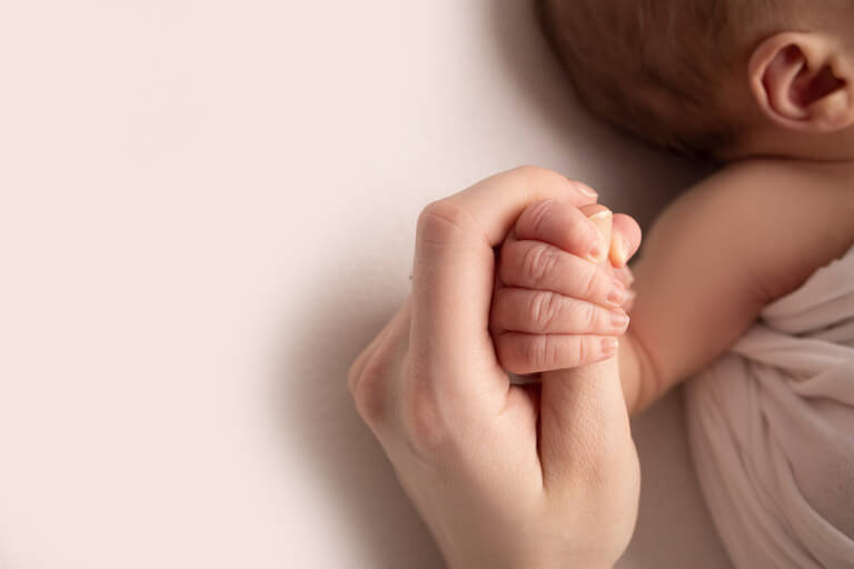 pic of a mother's hand holding the hand of her small infant who is sleeping