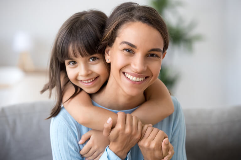 pic of a yoing girl on her mom's back and both smiling at the camera