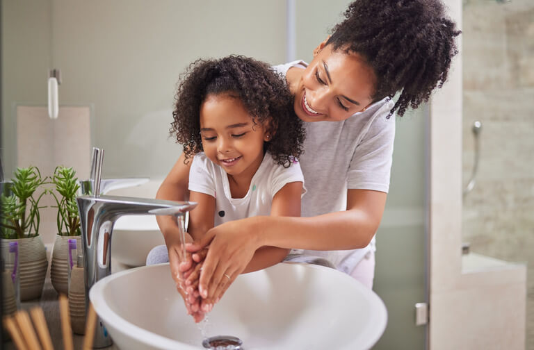 pic of smiling mom heling a smiling young girl wash her hands