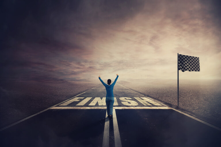 A person triumphantly raises their arms on a road leading to a checkered flag horizon, symbolizing achievement under a dramatic sky.