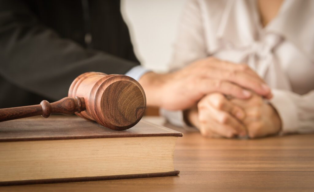 Close-up of a wooden gavel resting on a law book, with two people holding hands in the background, symbolizing legal support and family law representation.