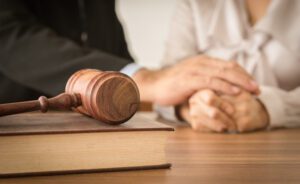 Close-up of a wooden gavel resting on a law book, with two people holding hands in the background, symbolizing legal support and family law representation.