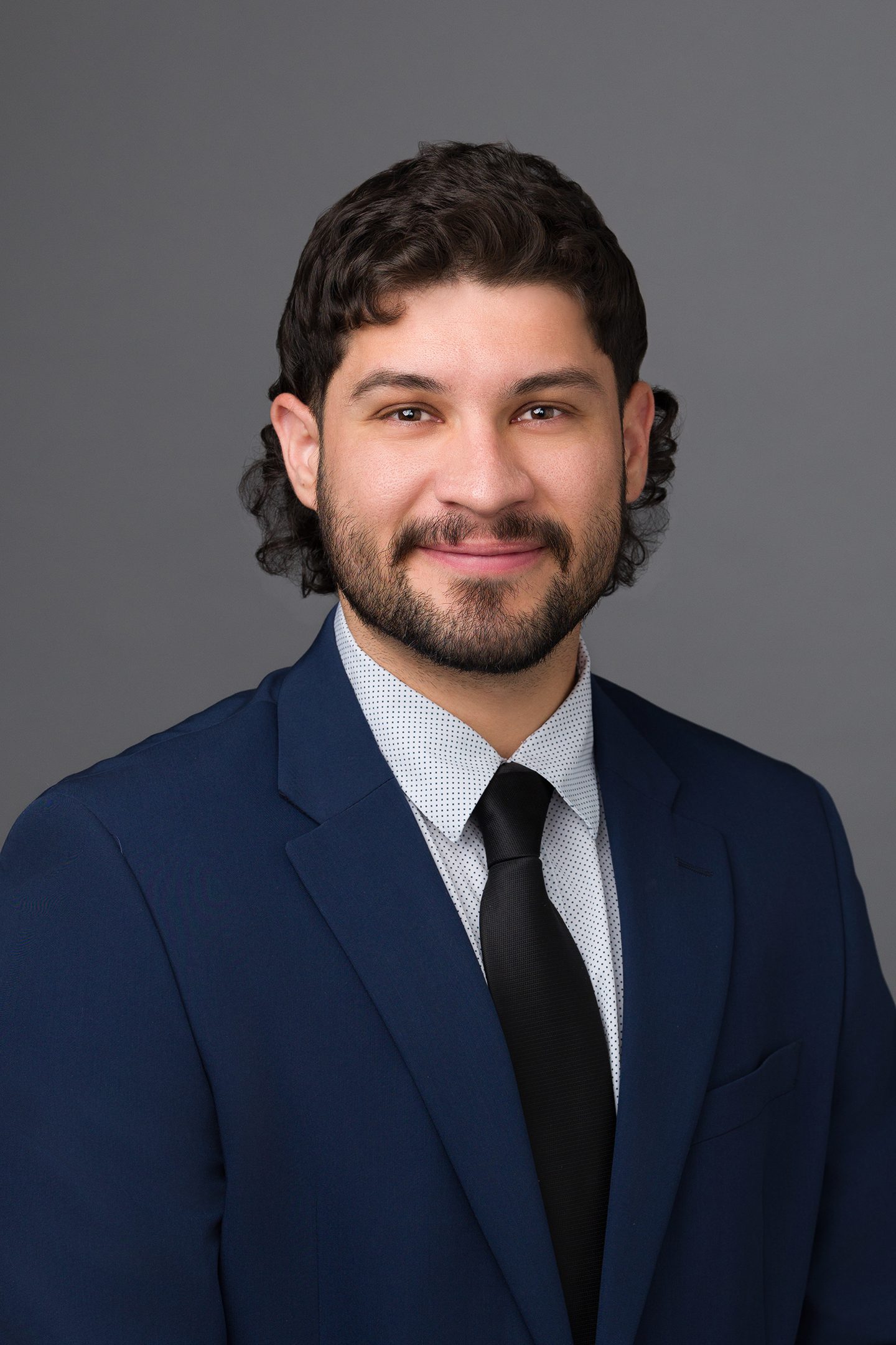 Professional headshot of Matt, legal assistant at Rosenblum Allen Law Firm, wearing a navy blue suit, white shirt, and black tie against a gray background.